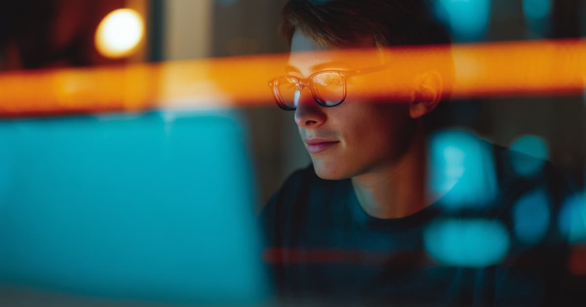 Person wearing glasses working at a laptop, seen through colourful blurred lights.