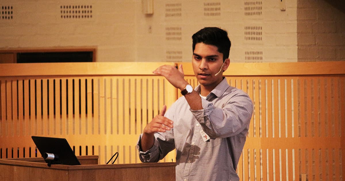 Josh David presents at Dyalog ’19, wearing a headset microphone and gesturing mid-explanation while standing at a podium. He is introducing his Easy GUI project.
