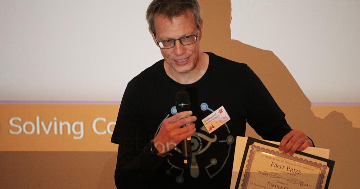 Professional Prize winner Torsten Grust holds a microphone and a certificate while speaking on stage at Dyalog '19.