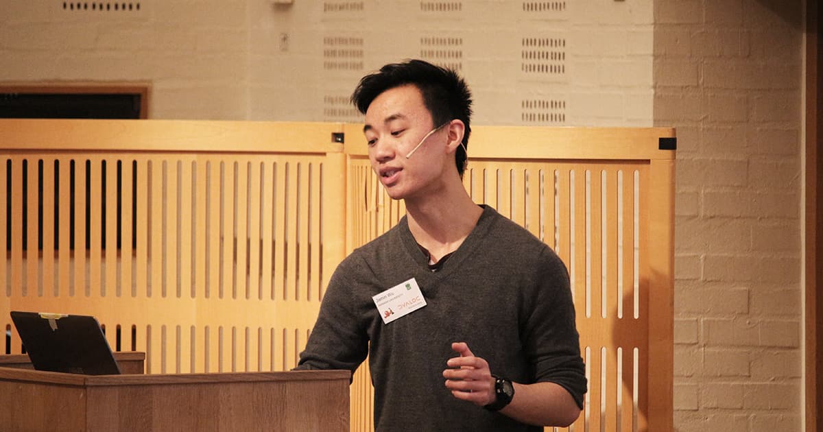 Grand Prize winner Jamin Wu presents on stage at Dyalog '19, speaking into a headset microphone while standing behind a podium.