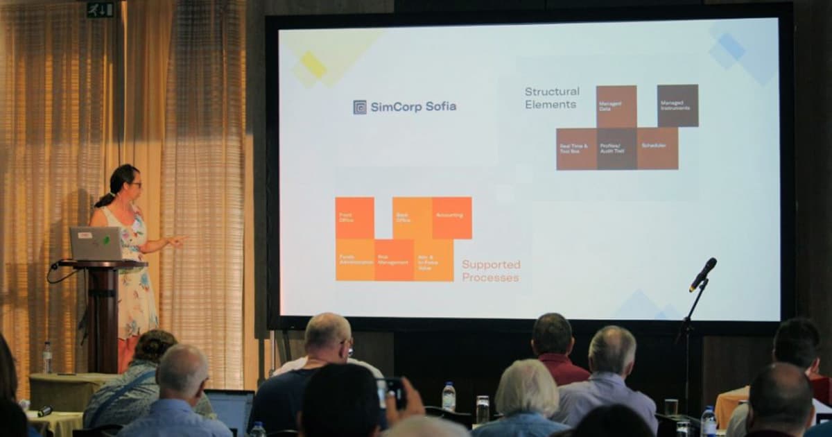 Elena Pavarotti presenting at Dyalog '22 in Olhão, Portugal, speaking about managing complexity in SimCorp Sofia while pointing to a slide displaying structural elements and supported processes.