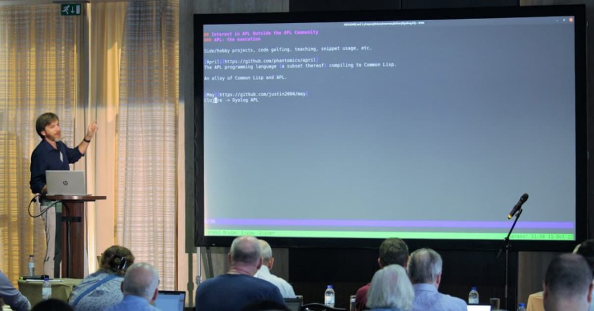 Justin Dowdy presenting at Dyalog '22 in Olhão, Portugal, discussing Notation as a Tool of Thought and data semantics, pointing toward a projected terminal window showing code and notes.