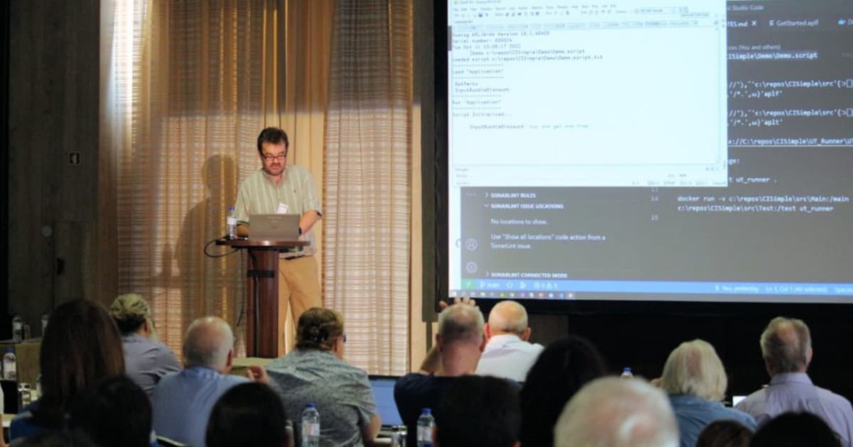 Lars Stampe Villadsen presenting at Dyalog '22 in Olhão, Portugal, discussing testing strategies while demonstrating code live on a large projected screen beside him.