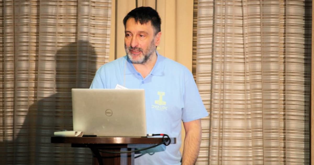 Michael Baas presenting at Dyalog '22 in Olhão, Portugal, demonstrating the ]DTest framework while standing at a podium with a laptop, wearing a light blue Dyalog shirt.