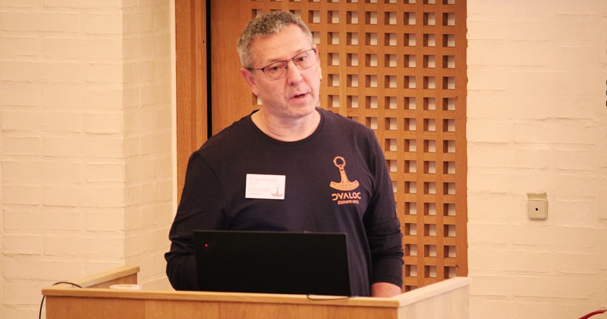 Morten Kromberg speaking at a podium during Dyalog ’23, wearing glasses and a dark Dyalog conference shirt with the event logo.
