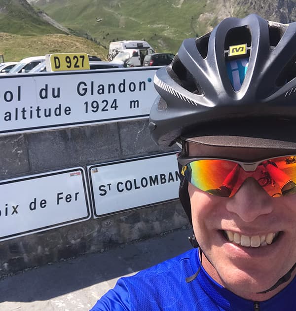 Stefan Kruger taking a selfie in cycling gear at the Col du Glandon, a mountain pass in the French Alps with an altitude of 1924 metres.