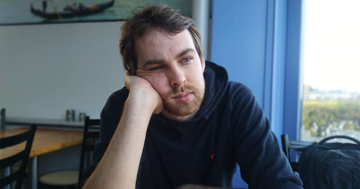 Karl Holt resting his head on his hand, gazing thoughtfully out the window of a café.