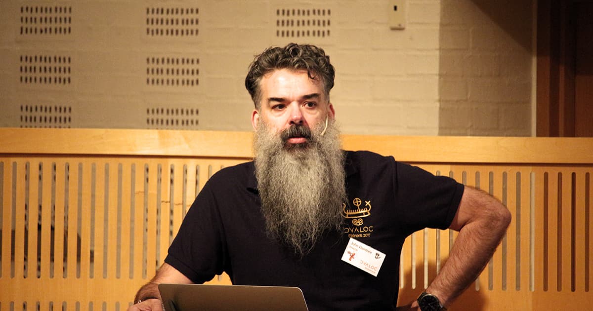John Daintree speaking at Dyalog ’19 in Elsinore, wearing a Dyalog-branded polo shirt with a laptop in front of him.
