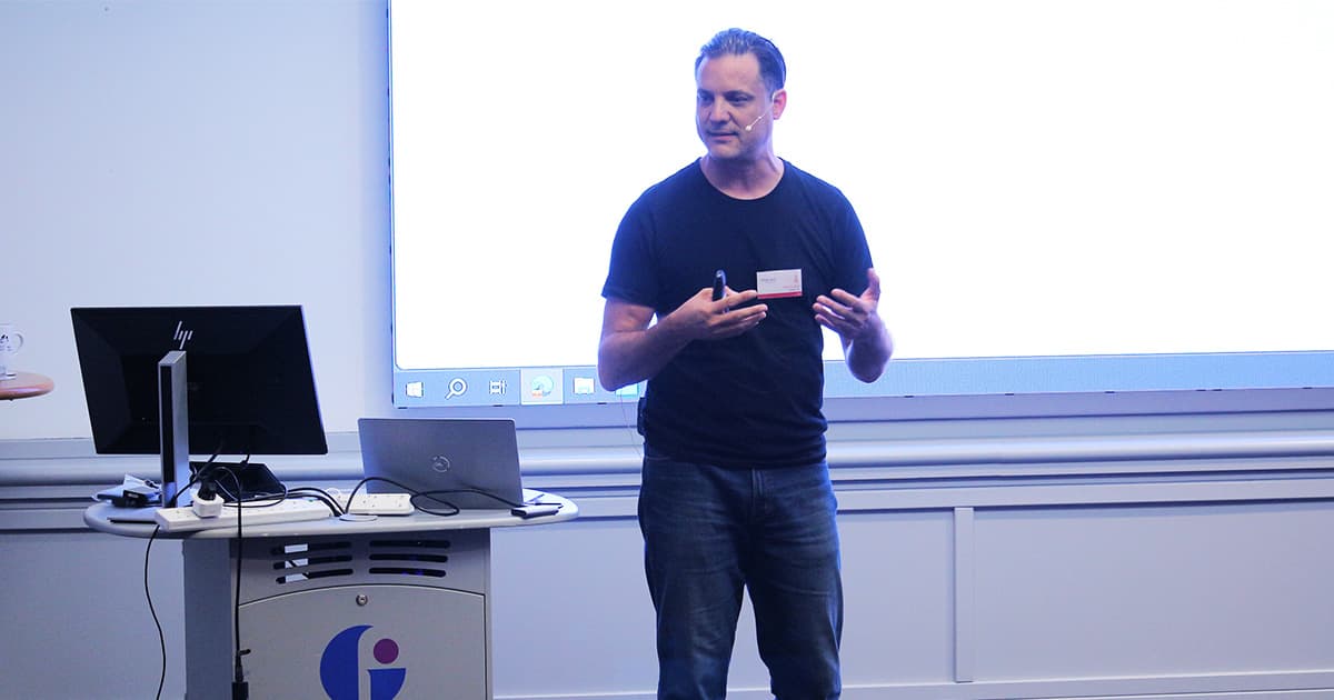 Oliver Lanz standing and speaking during his presentation at Dyalog ’24, with a laptop and monitor on the podium beside him.