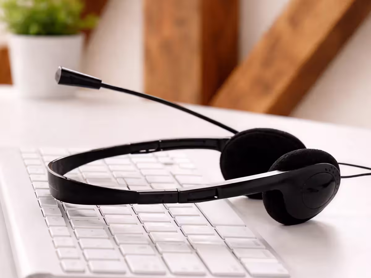 Black headset resting on a white keyboard on a desk, with a softly blurred warm office background.
