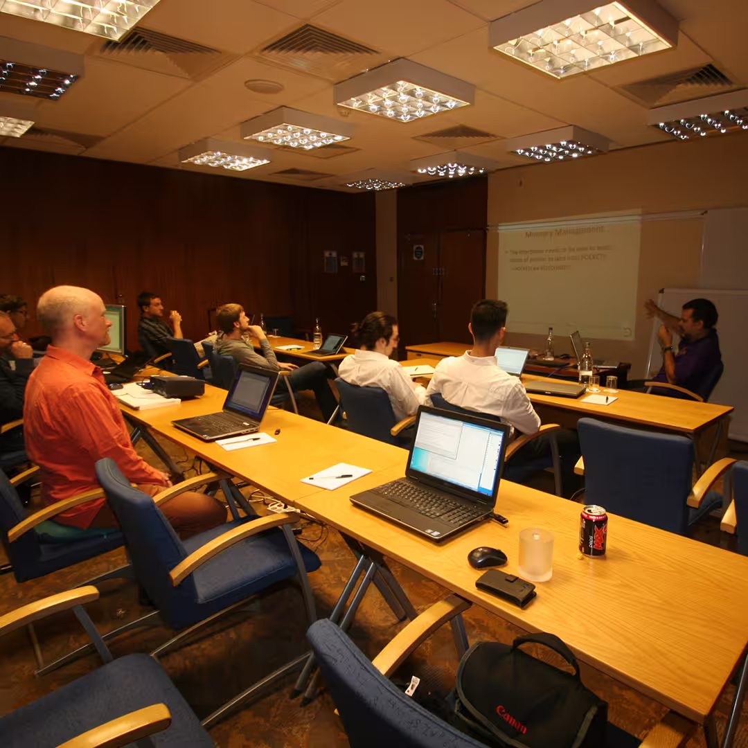 Dyalog '14 workshop session in Eastbourne, UK. A presenter is discussing memory management with a group of delegates seated at tables with laptops, notebooks, and drinks. A slide is projected on the wall behind the presenter.