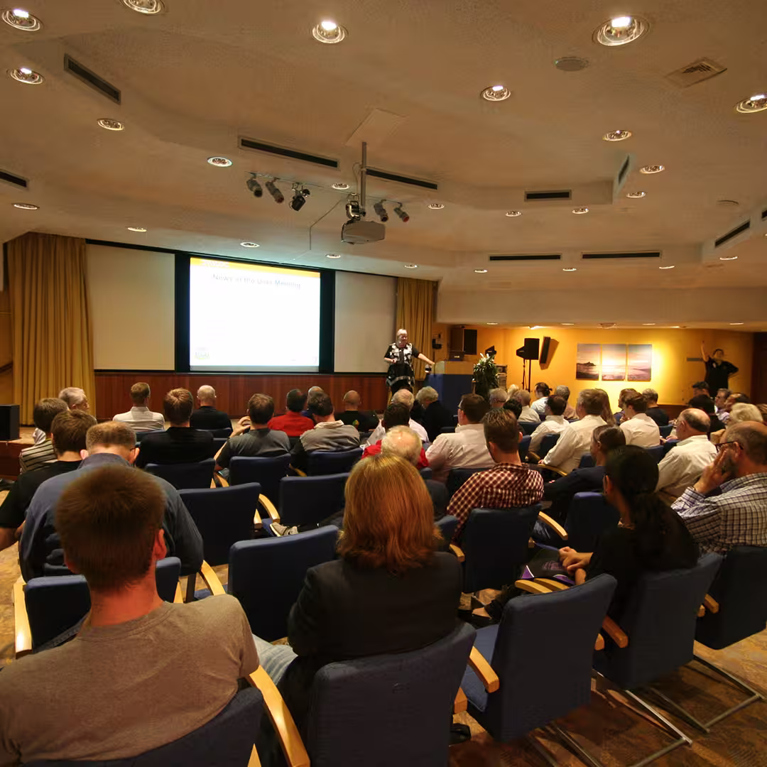 Gitte Christensen presenting at the Dyalog '14 event in Eastbourne, UK. She stands at the front of a conference room, speaking to an audience seated in blue chairs, with a presentation slide projected on the screen behind her.