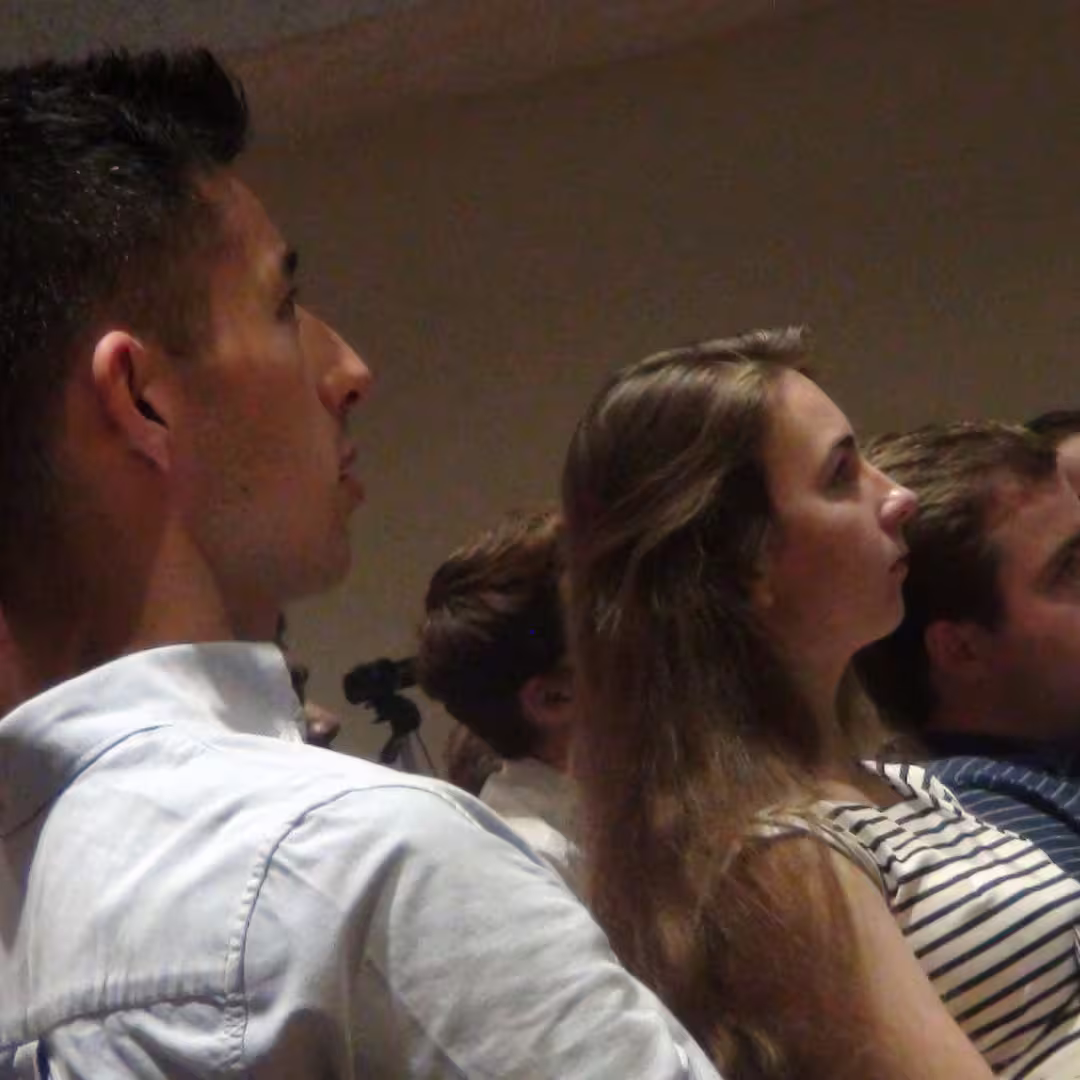 Dyalog '14 delegates seated in the audience, attentively listening to a presentation in Eastbourne, UK. A young man in a white shirt and a young woman in a striped top are in focus.