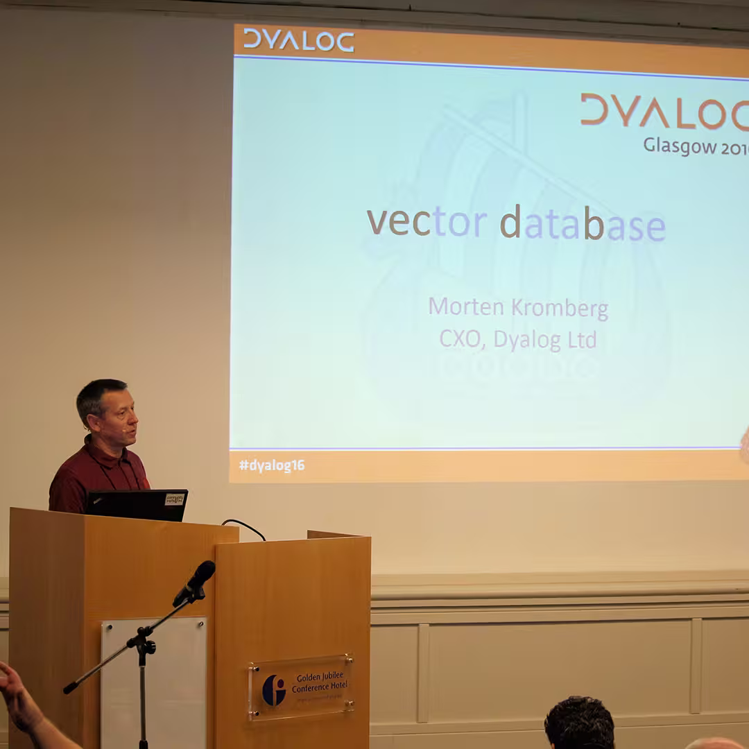 Morten Kromberg, CXO of Dyalog Ltd, standing at a wooden podium with a microphone, presenting a talk titled "Vector Database" at Dyalog '16 in Glasgow, Scotland. The presentation slide behind him features the Dyalog logo, a Viking ship graphic, and the hashtag #dyalog16. The podium has a plaque indicating the Golden Jubilee Conference Hotel.
