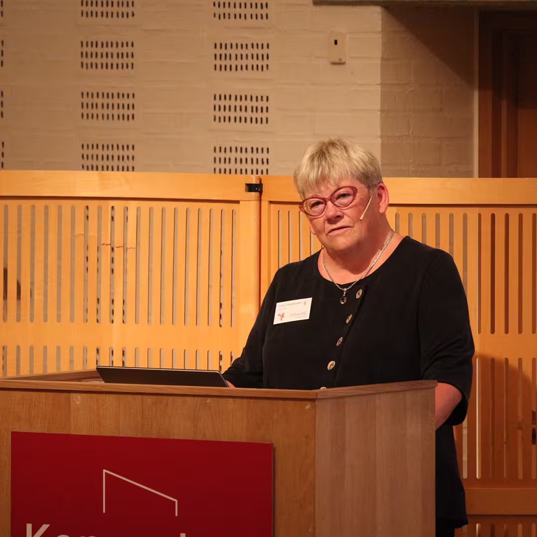 Gitte Christensen presenting at Dyalog '19, held at the Konventum Convention Centre in Elsinore, Denmark. She stands at the lectern, speaking into a headset microphone, with a laptop open in front of her.
