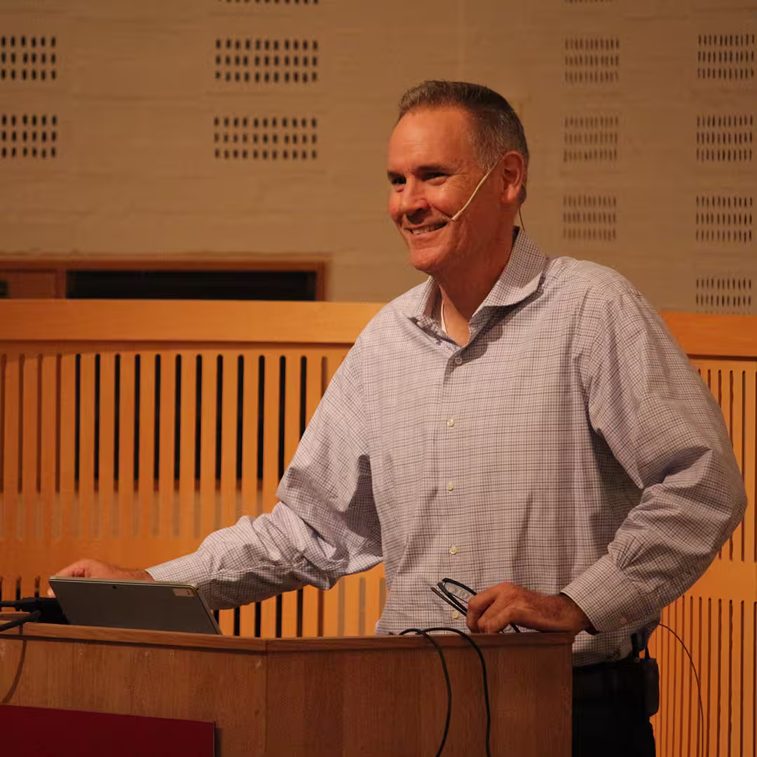 A delegate presenting at Dyalog '19, held at the Konventum Convention Centre in Elsinore, Denmark. He stands at the lectern, smiling while speaking into a headset microphone, with a tablet and presentation materials in front of him.