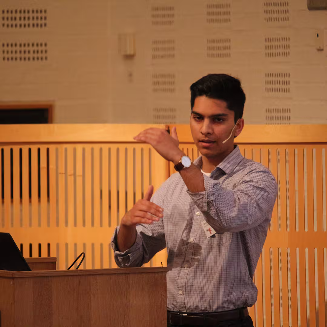 Josh David presenting at Dyalog '19, held at the Konventum Convention Centre in Elsinore, Denmark. He stands at the lectern, gesturing with both hands while speaking into a headset microphone.