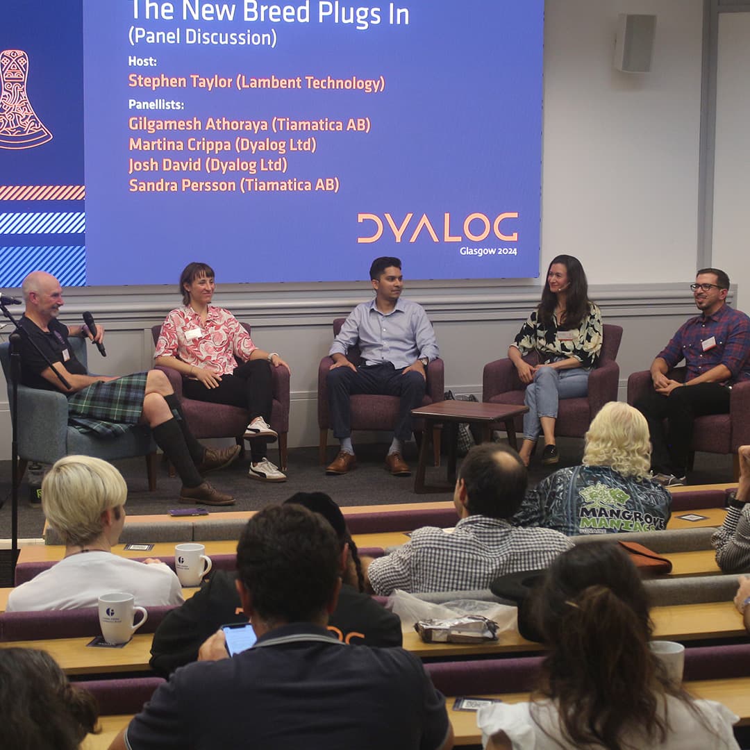 A panel discussion titled The New Breed Plugs In at Dyalog '24, held at the Golden Jubilee Hotel in Glasgow, Scotland. The host, Stephen Taylor, wearing a black shirt and a kilt, sits on the far left holding a microphone. The panellists, seated in a semi-circle, include Martina Crippa in a patterned blouse, Josh David in a light blue shirt, Sandra Persson in a floral top and jeans, and Gilgamesh Athoraya in a checked shirt and glasses. Behind them, a large screen displays the panel title, names, and affiliations of the participants, with the Dyalog logo and "Glasgow 2024" branding. The audience watches from tiered seating, with some taking notes or using their phones.