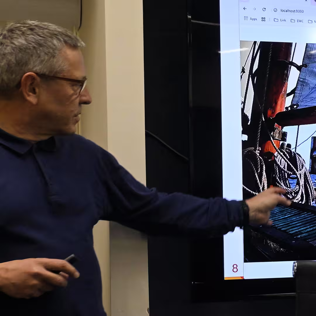 Morten Kromberg presenting at DYNA Spring 2025 in New York. He is gesturing toward a large screen displaying a photo of ropes aboard a ship. Morten is wearing a dark blue top and holding a presentation remote.